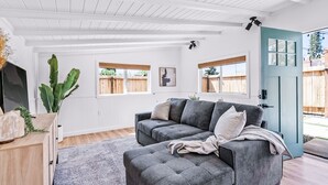Ein modernes Wohnzimmer mit einem grauen Ecksofa, einem Holzschrank und einer großen Pflanze.