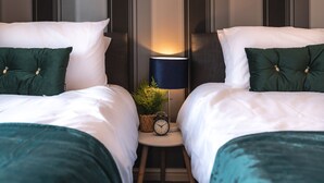 Een hotelkamer met twee bedden, elk voorzien van groene kussens en witte beddengoed. Tussen de bedden staat een klein tafeltje met een klok en een lamp.