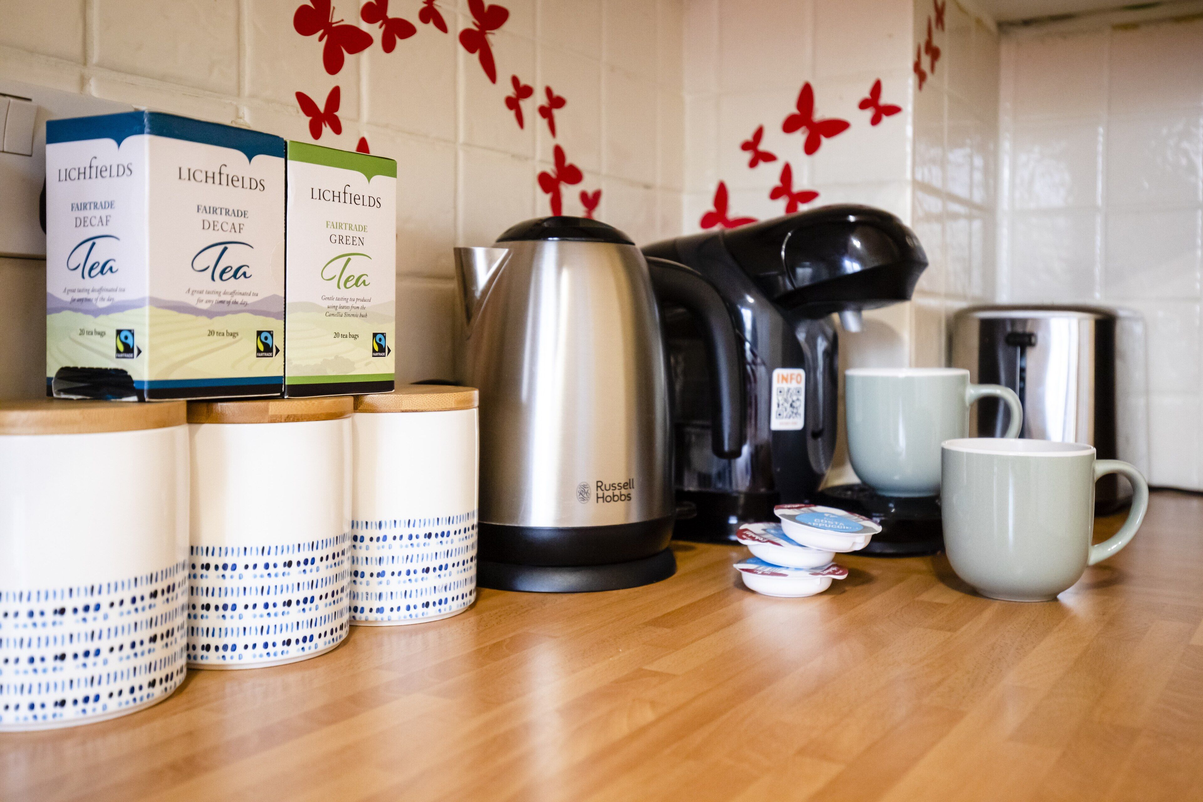 Una encimera de cocina con bolsitas de té, un hervidor, una cafetera y tazas.