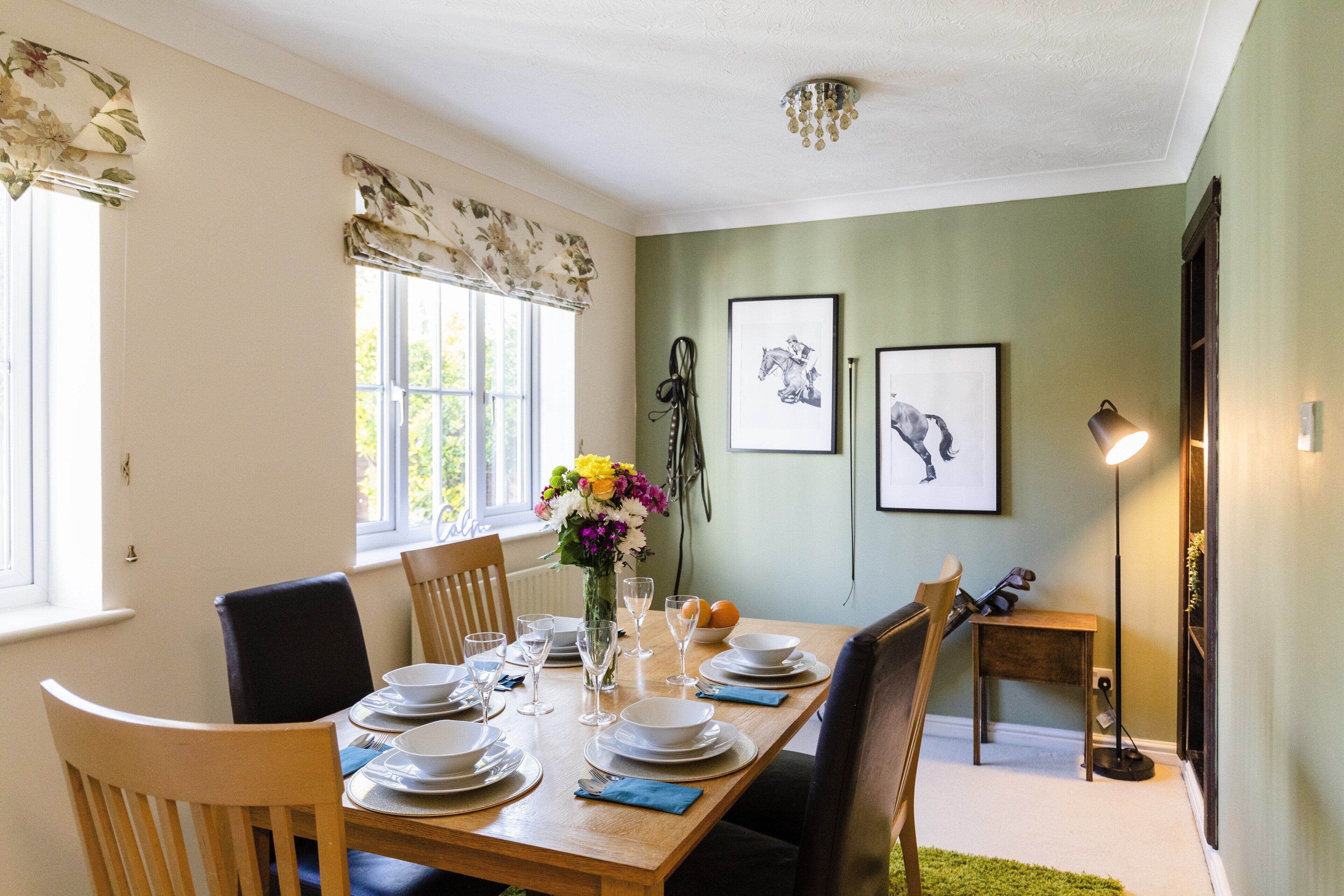 A dining room with a wooden table set for four, chairs, a vase with flowers, and framed pictures on the wall.