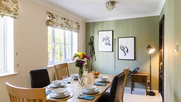 A dining room with a wooden table set for four, chairs, a vase with flowers, and framed pictures on the wall.