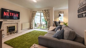 Een woonkamer met een open haard, een flatscreentelevisie, een groen tapijt, een grijze bank en een bord op de muur.