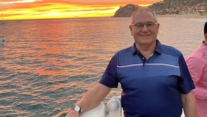 Ein Mann steht auf einem Boot und blickt auf eine Küstenstadt bei Sonnenuntergang.