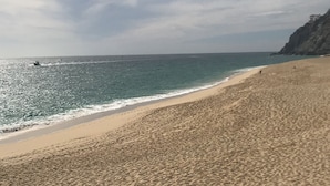 Ein sandiger Strand mit freiem Blick auf den Ozean und einer Felsküste im Hintergrund.