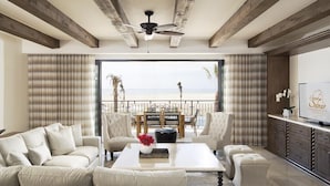 Ein geräumiges Wohnzimmer mit großem Fenster zum Strandblick, Deckenventilator und moderner Küchenzeile.