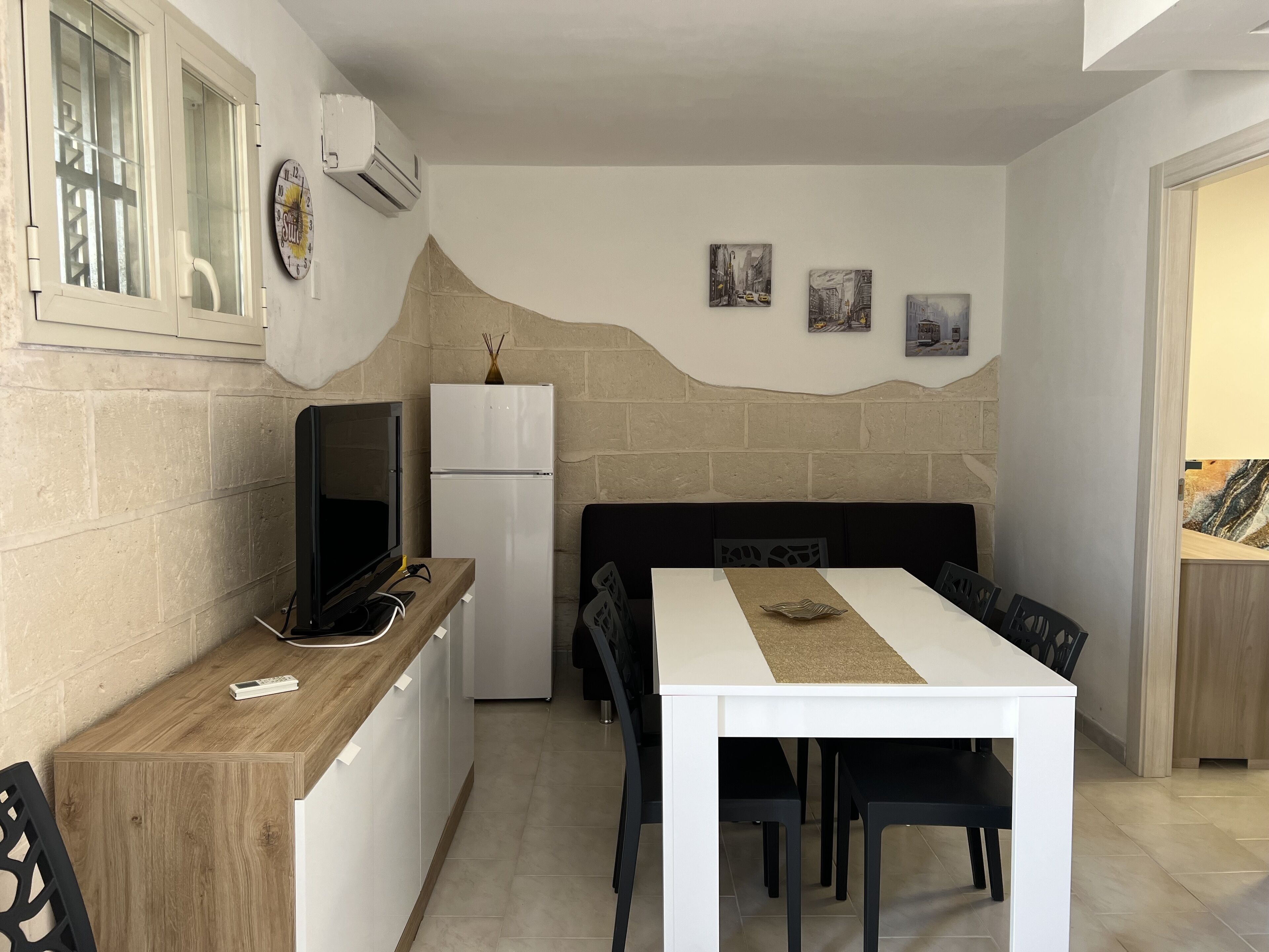 A compact kitchen with a built-in oven, a refrigerator, a wooden countertop, and a dining area with a table and chairs.