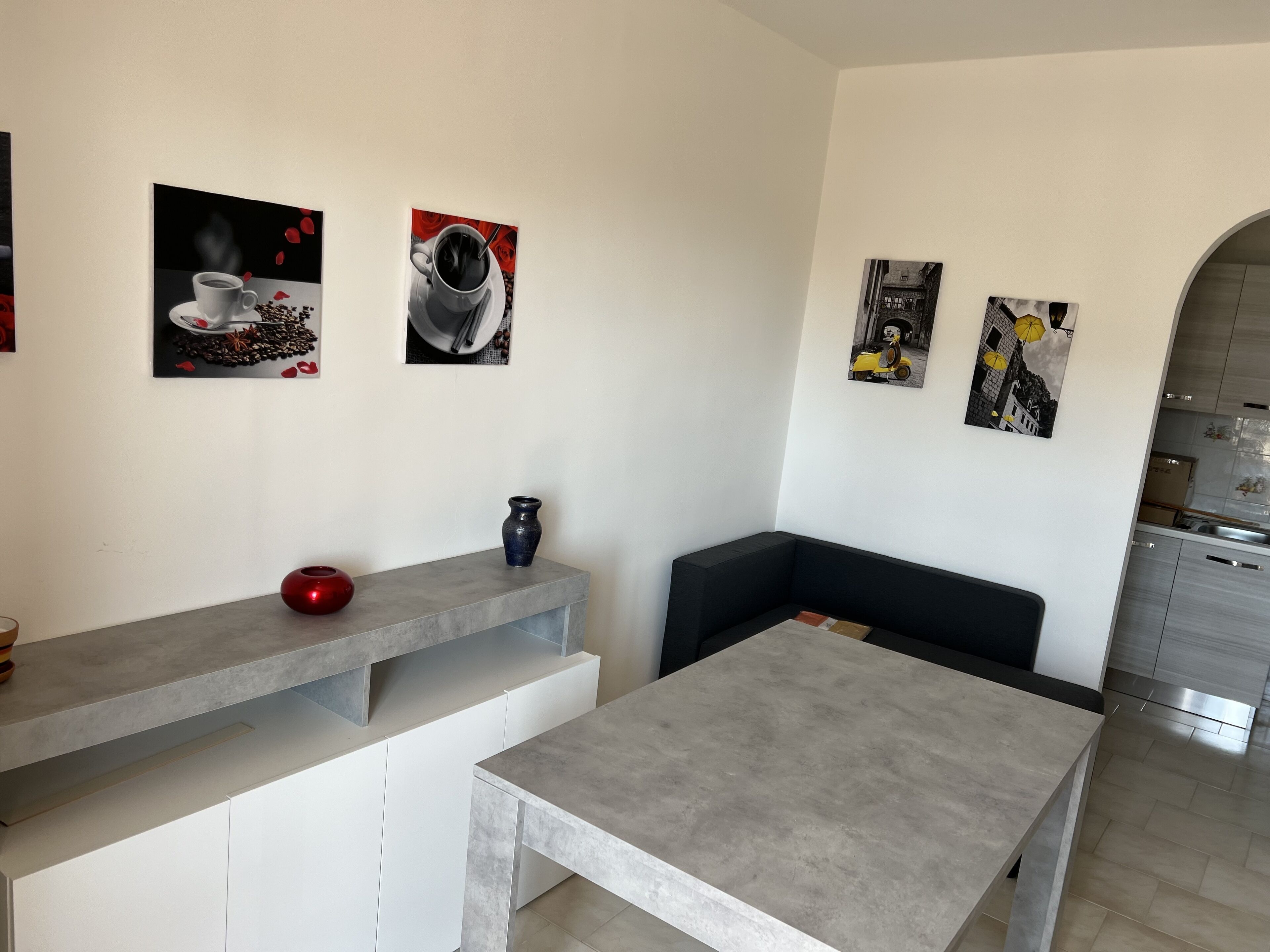 Een moderne keuken met een grijs aanrecht, een zwarte bank en een eettafel. Er hangen drie ingelijste foto’s aan de muur.