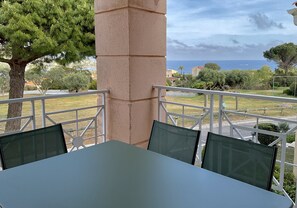 Ein Balkon mit Tisch und Stühlen, der auf eine Küstenlandschaft mit Bäumen und Gebäuden blickt.