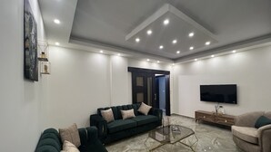 Una sala moderna con un sofá de color verde oscuro, una mesa de centro de vidrio y un sillón color beige.