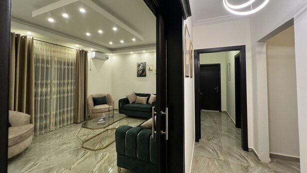 Una sala de estar moderna con un sofá verde oscuro, un sillón color beige y una mesa de centro de vidrio.