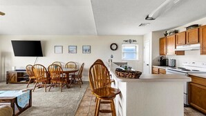 Una cocina moderna con armarios de madera, una isla central y un comedor con sillas de madera.