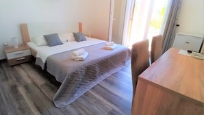 A hotel room with a bed, a wooden nightstand, a desk, and a window with curtains.