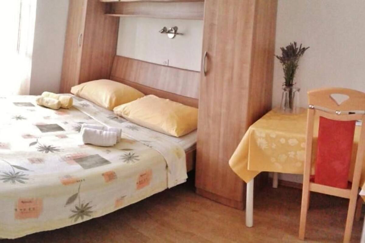 A bedroom with a bed, a bedside table, a chair, and a small table with a vase.