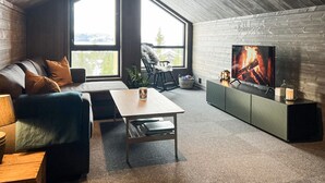 Ein modernes Wohnzimmer mit großem Fenster, einer Couch, einem Couchtisch und einem Fernseher an einer Holzwand.