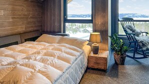 Ein gemütliches Zimmer mit einem großen Bett, einer Lampe, einem Sessel und Blick auf verschneite Berge.