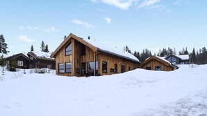 Eine Holzhütte mit großen Fenstern und einem geneigten Dach, umgeben von Schnee und Bäumen.