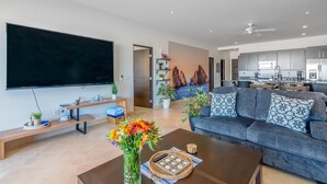 Ein modernes Wohnzimmer mit Flachbildfernseher, einer Couch, einem Couchtisch und einem Essbereich mit einer Küche im Hintergrund.