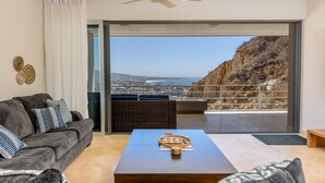 Ein modernes Wohnzimmer mit einer Couch, einem Couchtisch und Blick auf eine Küstenlandschaft durch große Glasfenster.