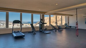 Ein Fitnessstudio mit unterschiedlichen Trainingsgeräten, großen Fenstern und einem Blick auf die Stadt sowie einer hohen Decke.