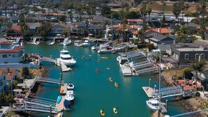 A marina with boats docked, kayaks on the water, and a hilly landscape in the background.