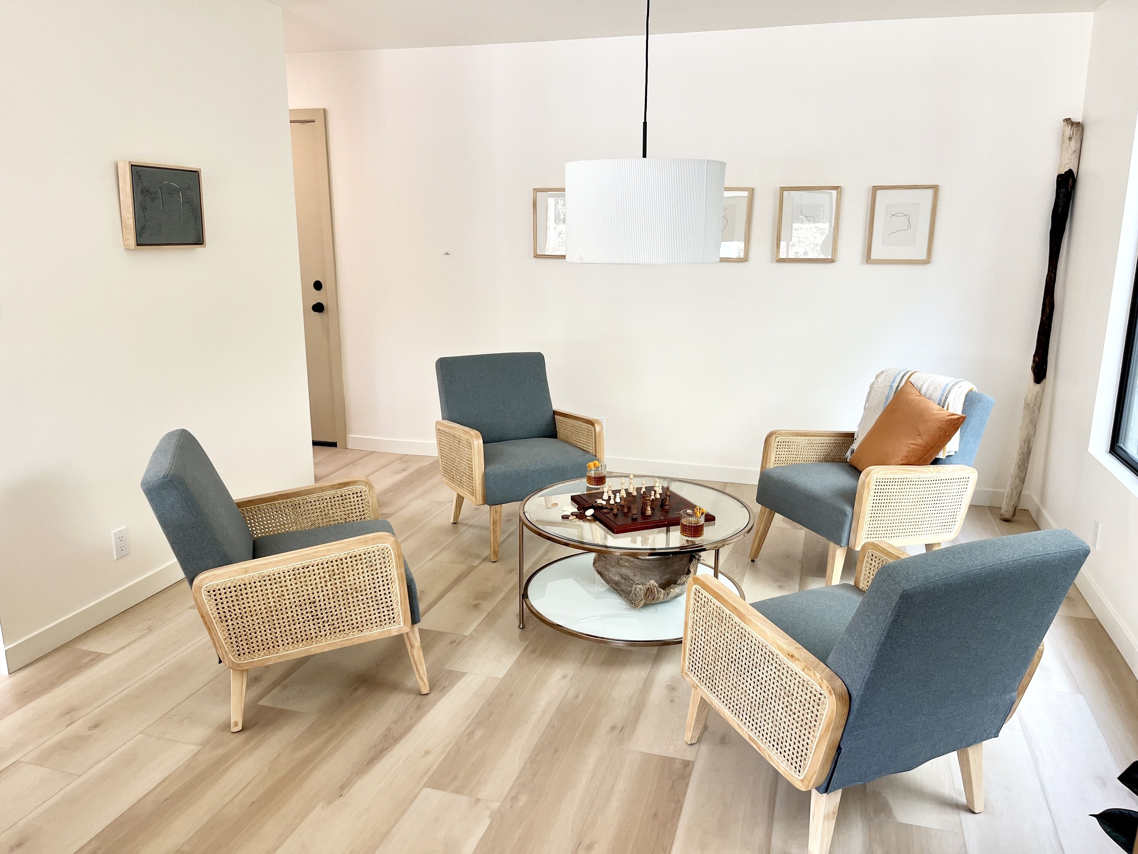Un salón moderno con una mesa de centro redonda de cristal, sillones tapizados en azul y una lámpara colgante.