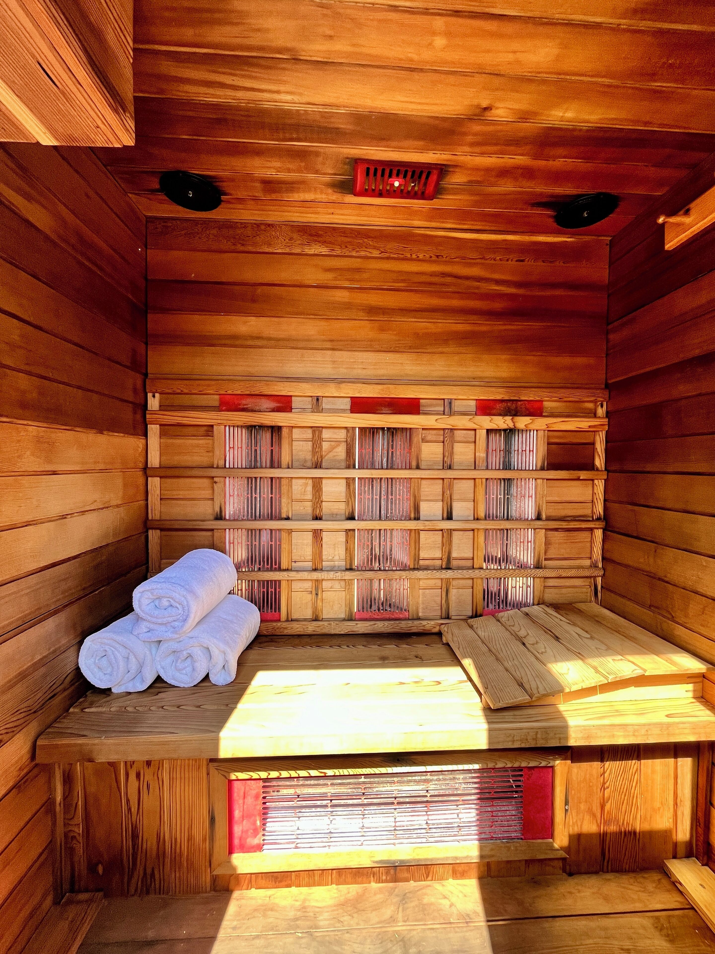 Eine Sauna mit Holzwänden und -bänken, einem Handtuchhalter und einem sichtbaren Bedienfeld.
