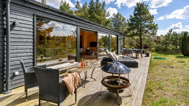 A modern outdoor deck with a fire pit, seating, and a glass door leading to an interior space. - 3 bedroom cozy home in Blokhus (Blokhus)