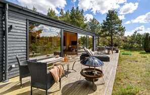 En moderne terrasse udendørs med pejse, siddepladser og en glasdør til et indre rum.