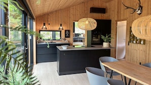 A modern kitchen with wooden walls, a central island, and pendant lighting. - 3 bedroom cozy home in Blokhus (Blokhus)