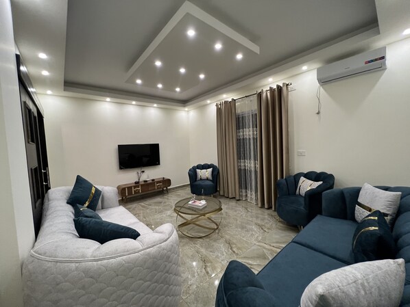 A modern living room with a sofa set, a coffee table, and a flat-screen TV mounted on the wall.