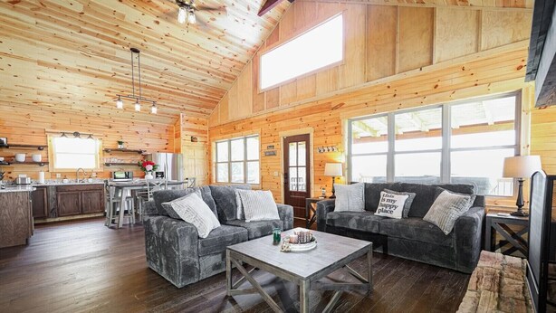 A spacious living room with two grey sofas, a coffee table, and a kitchen area in the background.