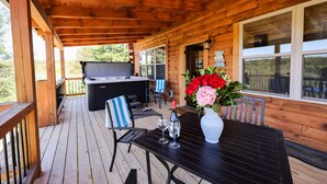 A wooden deck with a barbecue area, a table with a vase of flowers, and a view of the surrounding forest.