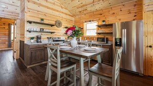 A wooden cabin interior with a kitchen featuring a stainless steel refrigerator, wooden cabinets, and a dining table set for four.