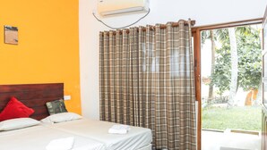A hotel room with two beds, a red pillow, a white pillow, a brown curtain, and a view of greenery outside. - New Tristar Beach Hotel (Arugam Bay)