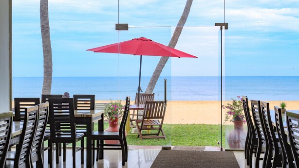 A dining area with a view of the beach, featuring wooden chairs and a red umbrella. - New Tristar Beach Hotel (Arugam Bay)