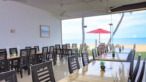 A dining area with tables and chairs, a ceiling fan, and a view of the beach. - New Tristar Beach Hotel (Arugam Bay)