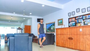 A hotel lobby with a reception desk, seating area, and a television mounted on the wall. - New Tristar Beach Hotel (Arugam Bay)