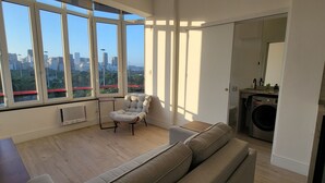 A modern living room with a large window, a sofa, a chair, and a washing machine. - Ocean and City Views (Rio de Janeiro)