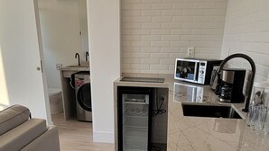 A modern kitchen with a marble countertop, a coffee maker, and a microwave. There is a wooden stool and a sofa in the living area. - Ocean and City Views (Rio de Janeiro)