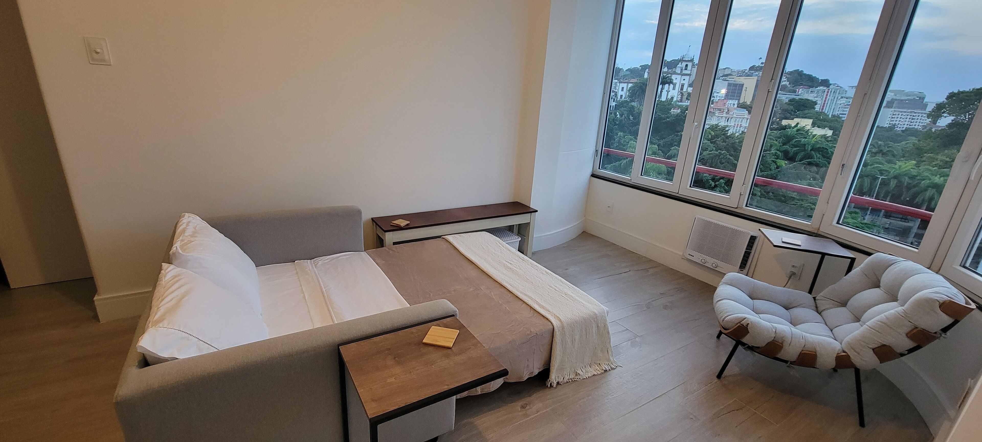 Une chambre moderne avec un lit, une chaise, une petite table et une grande fenêtre donnant sur la ville.