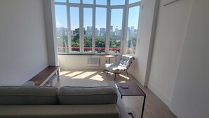 A modern living room with a large window, a grey sofa, a white armchair, and a small table. - Ocean and City Views (Rio de Janeiro)