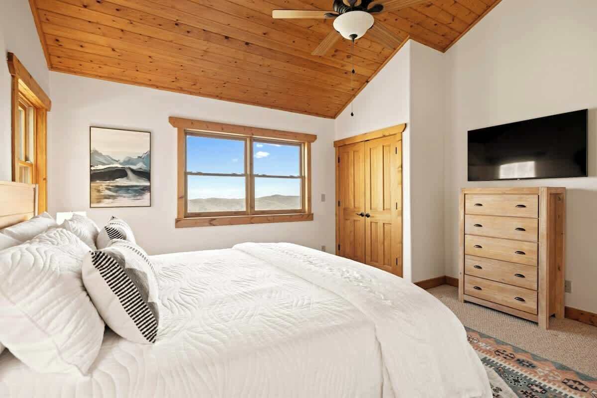 Une chambre à coucher comprenant un lit, un ventilateur de plafond, une fenêtre avec vue, une armoire en bois et un téléviseur.