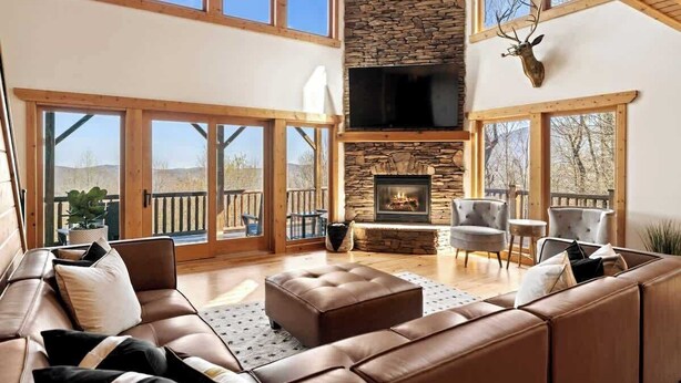 A spacious living room with a stone fireplace, leather sofas, and large windows. - Private Community~5 Bedrooms~Loaded~Amazing Mountain View’s-Jacuzzi-Game Room (Seven Devils)