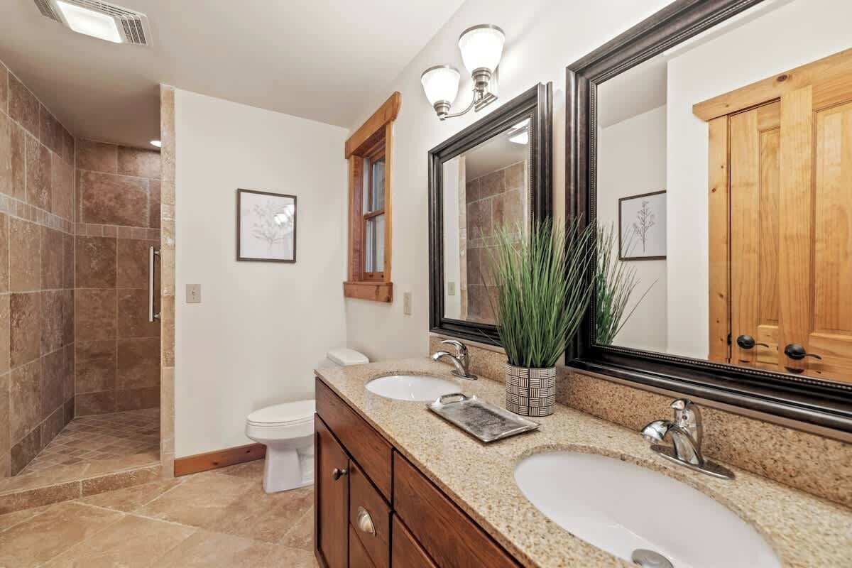 Une salle de bain dotée d’un meuble-lavabo à deux vasques, d’un grand miroir et d’un espace douche.