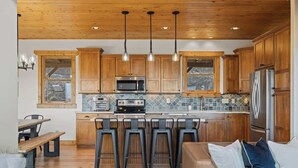 A kitchen with wooden cabinets, a stainless steel refrigerator, a microwave, and a stove. There are four bar stools and a bench. - Private Community~5 Bedrooms~Loaded~Amazing Mountain View’s-Jacuzzi-Game Room (Seven Devils)
