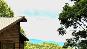 A wooden cabin with a balcony overlooking a dense forest and distant mountains. - Private Community~5 Bedrooms~Loaded~Amazing Mountain View’s-Jacuzzi-Game Room (Seven Devils)