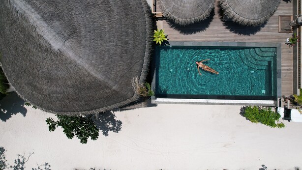 An aerial view of a swimming pool with two thatched umbrellas, surrounded by a wooden deck and greenery. - Island Luxury Boutique Hotel - Fulhadhoo (Fulhadhoo)