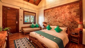 A bedroom with a wooden ceiling, a large bed with green pillows, a wooden headboard, a bedside table, and a window with a view of greenery. - Island Luxury Boutique Hotel - Fulhadhoo (Fulhadhoo)