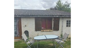 Ein Haus mit Ziegeldach, einem kleinen Fenster mit Fensterläden und einem Tisch mit Stühlen im Vorgarten.