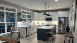 Une cuisine moderne avec des meubles blancs, un îlot central, un réfrigérateur en acier inoxydable et un coin repas comprenant une table et des chaises en bois.